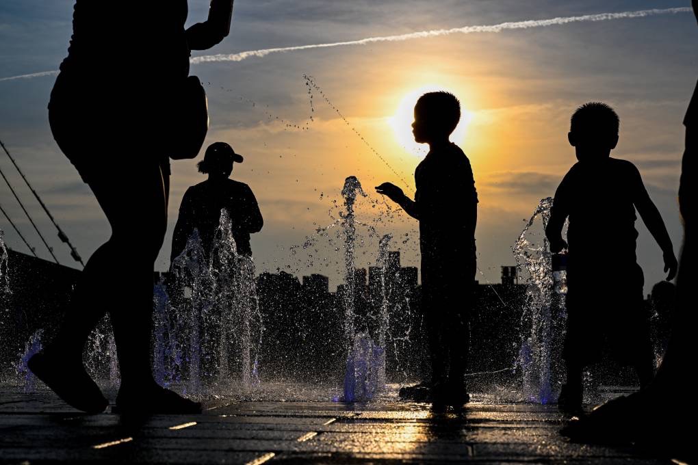 With the Manhattan skyline in the background as the sun set during a heat wave on July 24, 2022, children cooled off by playing in a fountain in Domino Park, Brooklyn, a borough of New York City. (Alexi Rosenfeld/Getty Images)